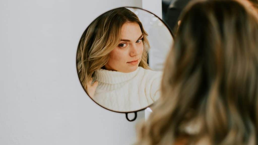 A woman looking at her reflection in a round mirror indoors.