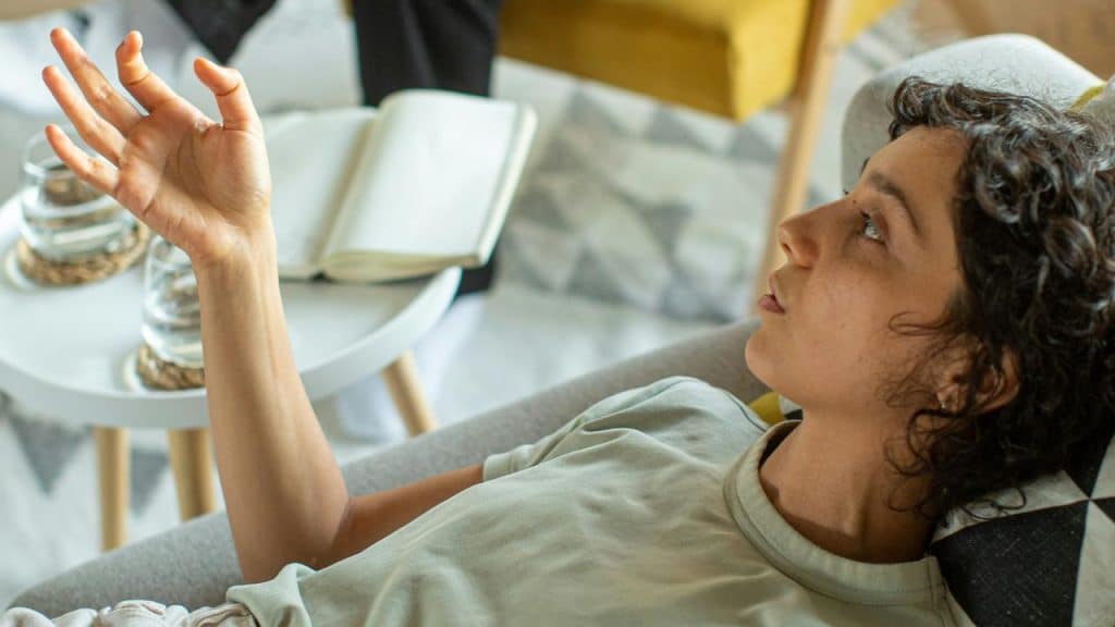 A woman lying on a couch and raising her hand while speaking.