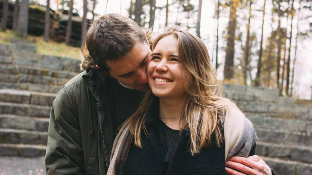 A happy couple sharing an affectionate moment outdoors with trees in the background.