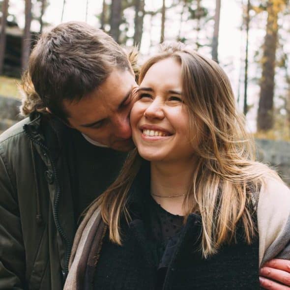 A happy couple sharing an affectionate moment outdoors with trees in the background.