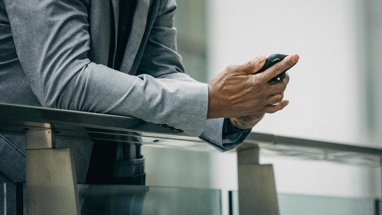 A person holding a smartphone while leaning on a balcony.