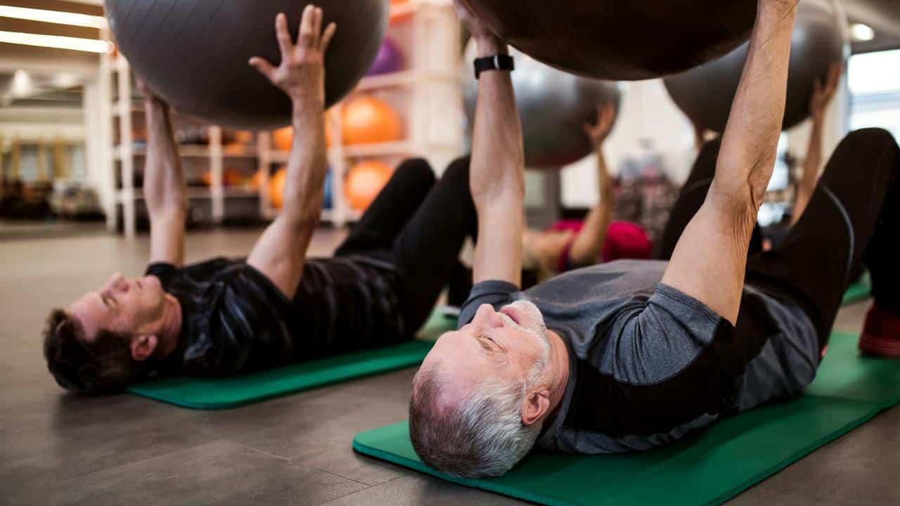 An older man lifting an exercise ball in a gym.