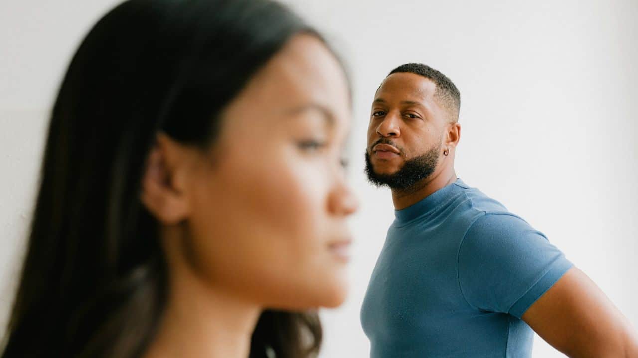 A man in a blue shirt looks toward a woman who is blurred in the foreground.
