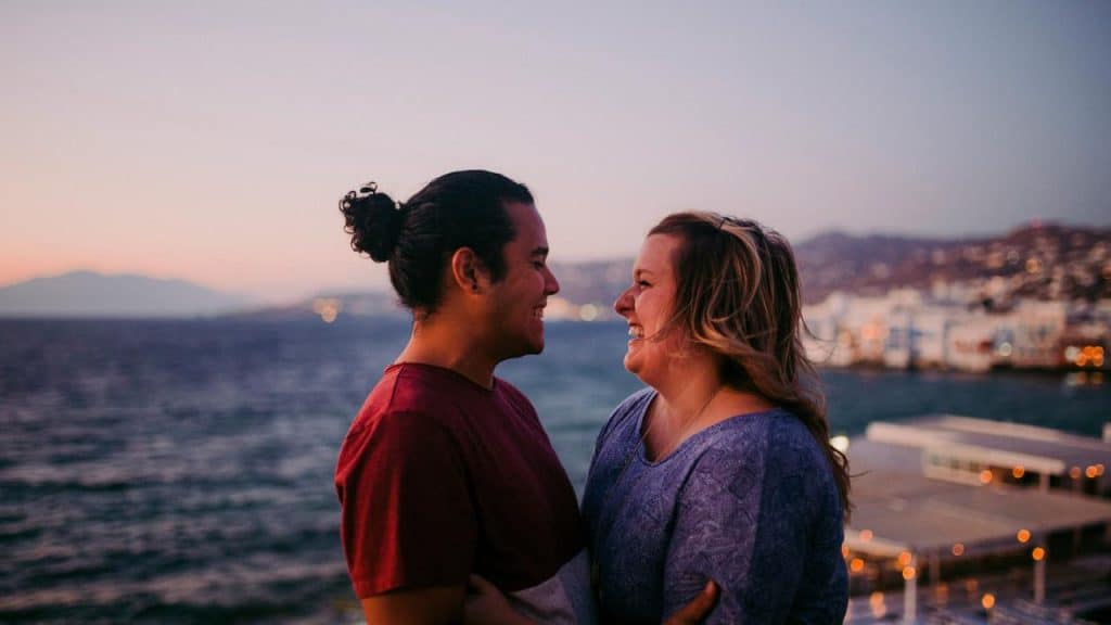 A couple smiling at each other by the ocean at sunset.