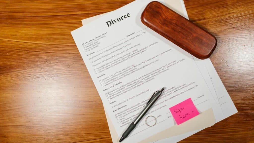 Legal divorce documents and a pen lie on a wooden table with a pink note.