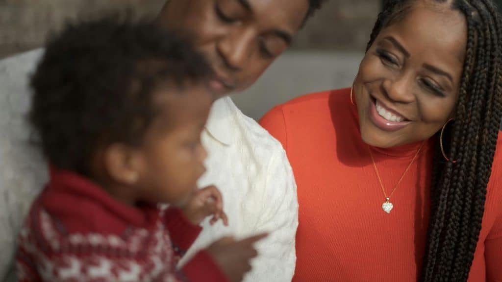 A smiling couple looking affectionately at a baby between them.