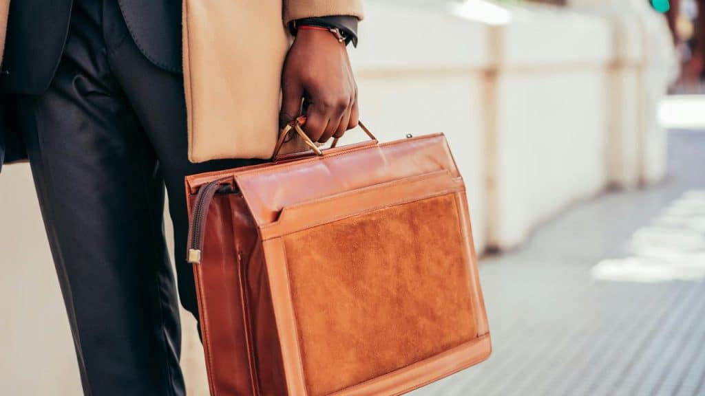 A person holding a brown leather briefcase while walking outdoors.