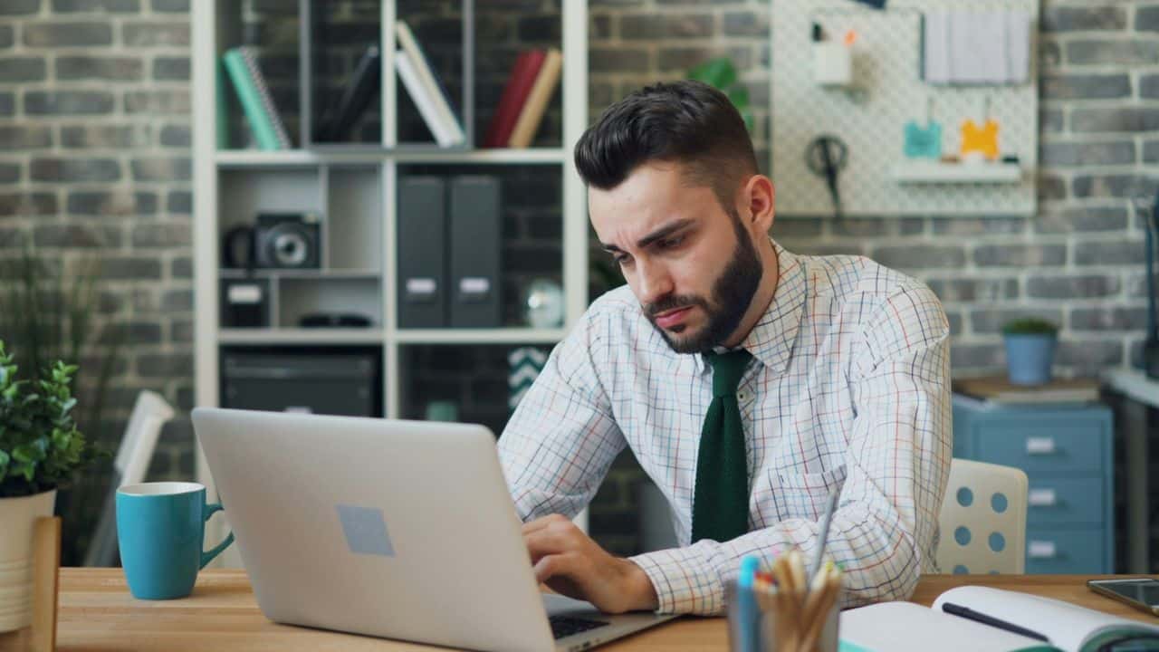A man in a tie looks intently at a laptop screen while typing on the keyboard.
