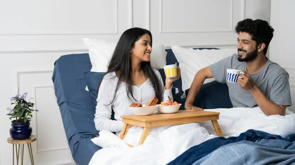 A couple smiling at each other while having breakfast in bed.