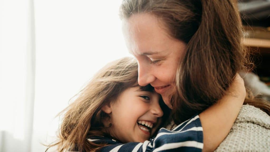 A mother hugging her smiling child indoors.