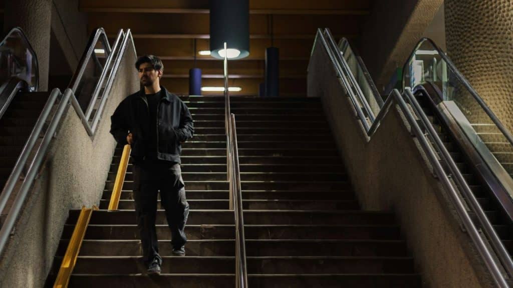A man in a black jacket walks down a wide staircase between two escalators.