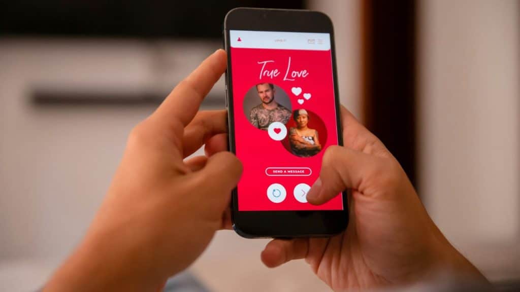 Hands hold a smartphone displaying a red dating app screen with two circular profile photos.