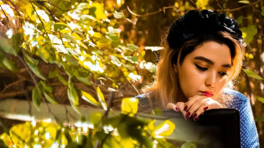 A young woman with a black floral headband rests her chin on her hands outdoors.