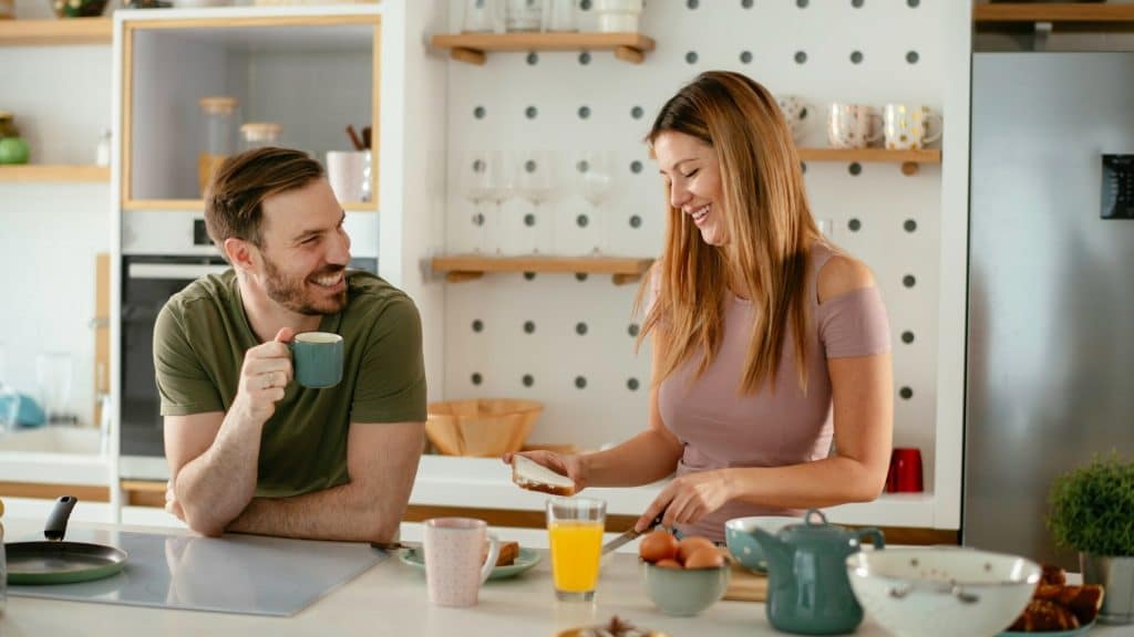 A couple having a conversation while preparing breakfast in the kitchen.