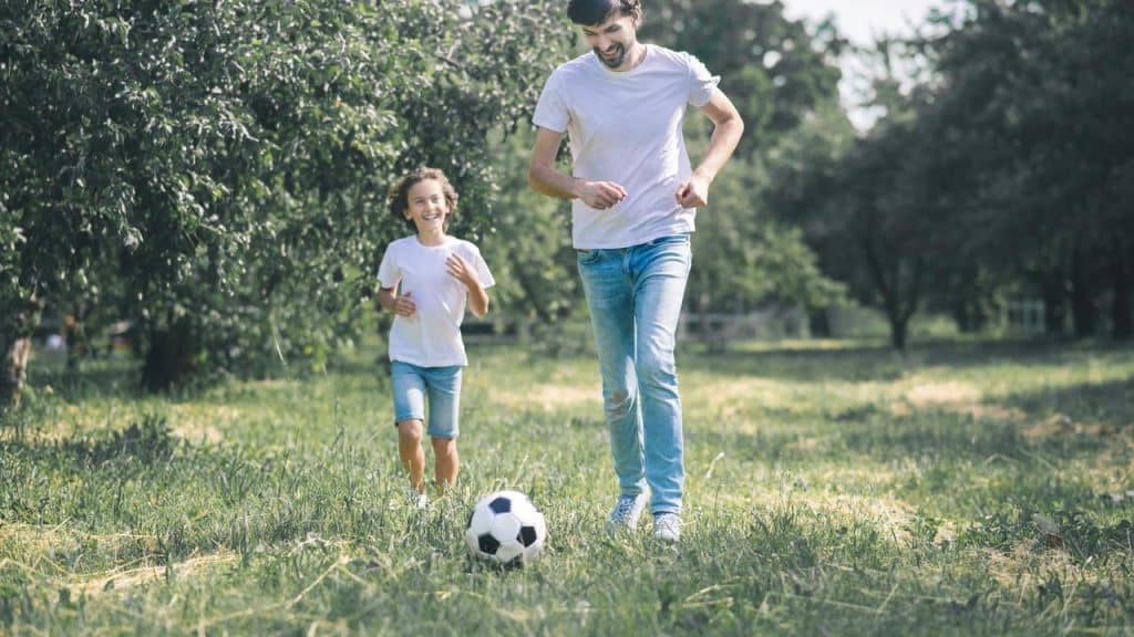 A father playing soccer with his child outdoors.