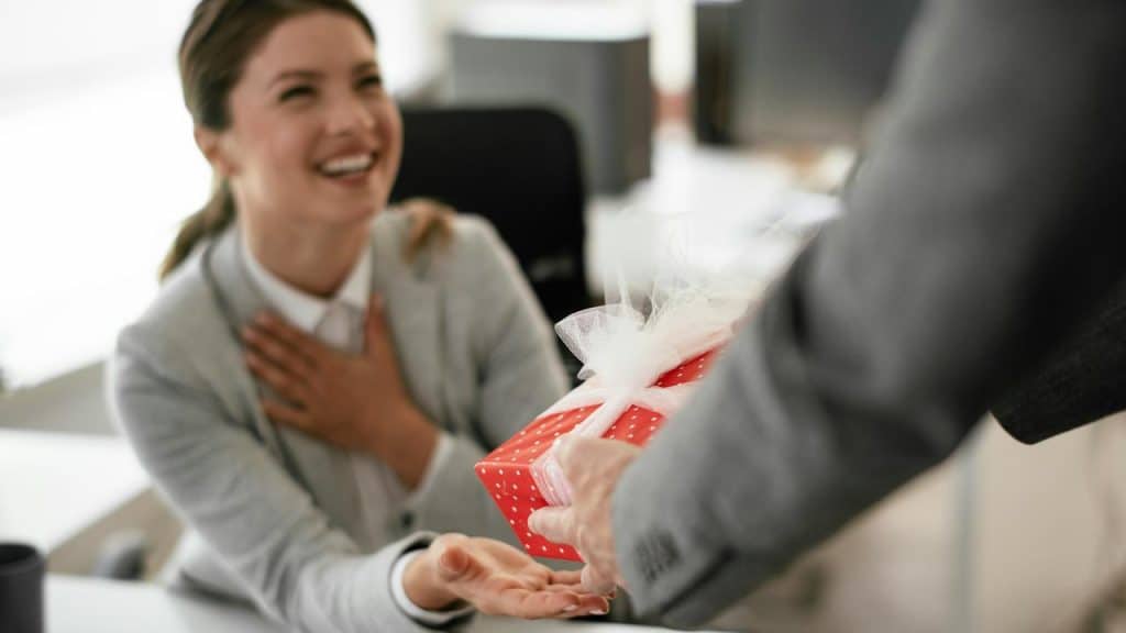 A smiling woman receives a wrapped gift box from someone.