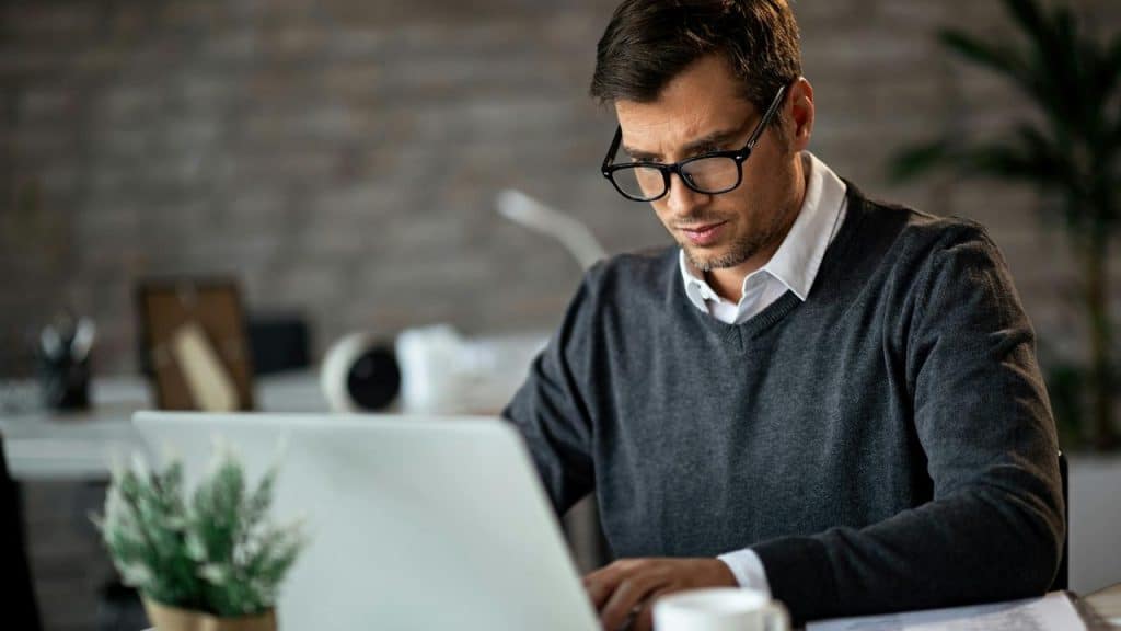 A man in glasses working on a laptop at a desk.