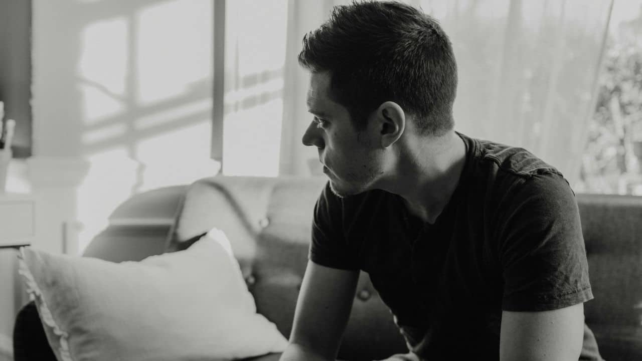 A man in profile sits alone on a sofa in a black and white photograph.