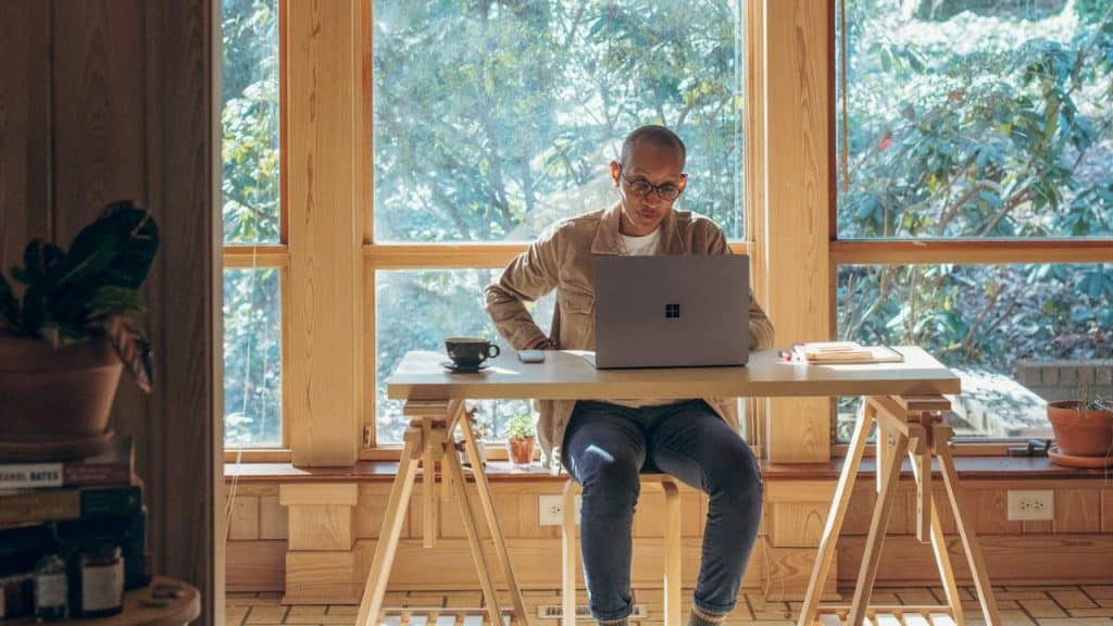 A person wearing glasses and a tan jacket works on a laptop at a desk.