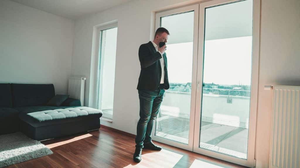 A man in a blazer and jeans stands in a room holding a smartphone.