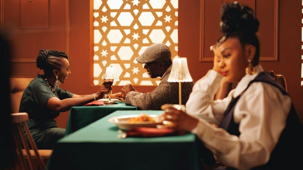 A woman looks away while a man and woman talk at a nearby dinner table.