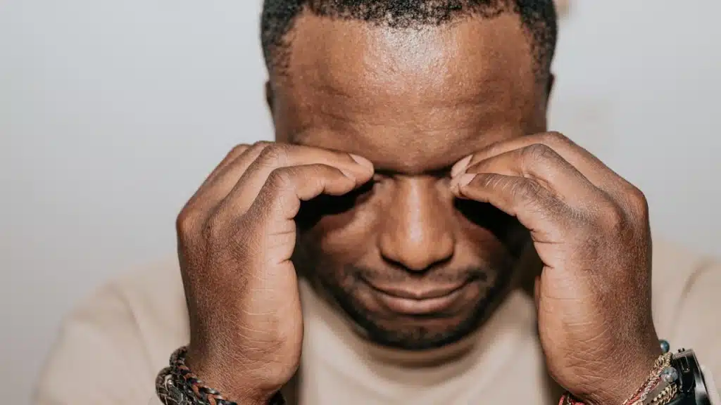 A man squeezing his closed eyes with his fingers and looking upset.