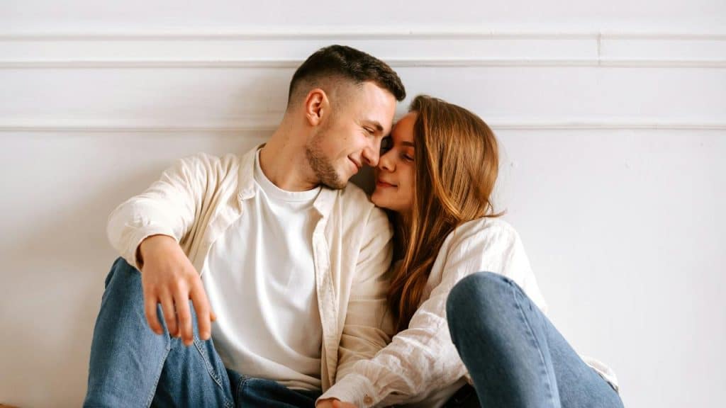 A couple sitting close together indoors while sharing an affectionate smile.