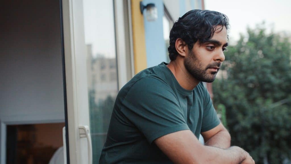 A man with dark hair looks off into the distance while leaning on a balcony.