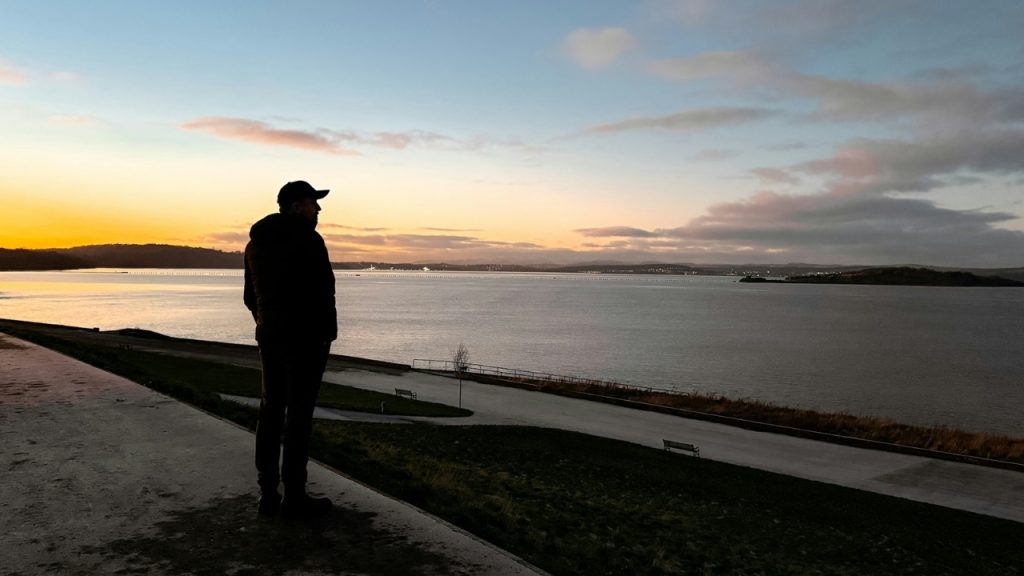 A silhouette of a man looking out over a wide body of water at sunset.