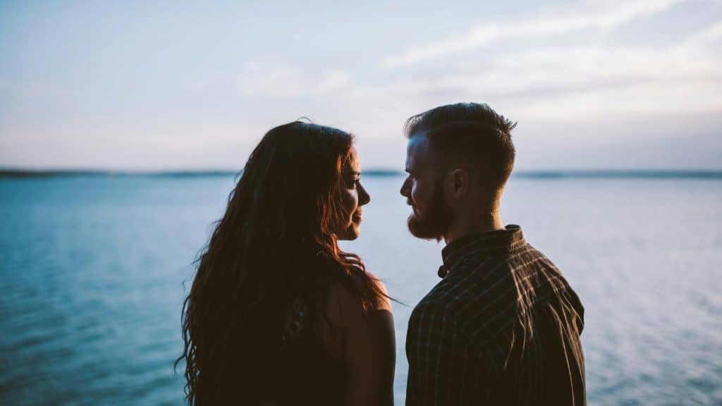 A couple silhouetted by a lakeshore at dusk.