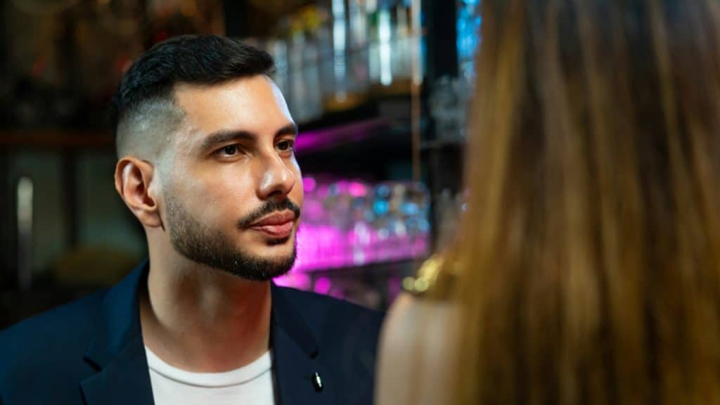 A man in a dark jacket looks attentively at a woman with long, brown hair.