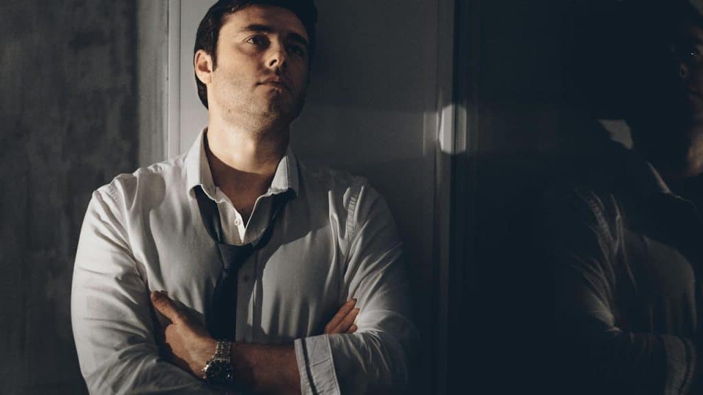 A person stands with arms crossed, wearing an unbuttoned dress shirt.