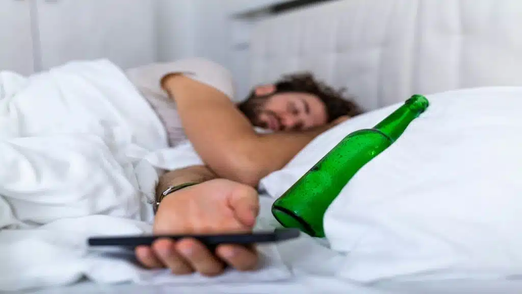 A drunk man with an alcohol bottle in bed