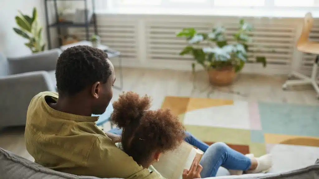 A parent and child sitting together on a couch, reading a book at home.
