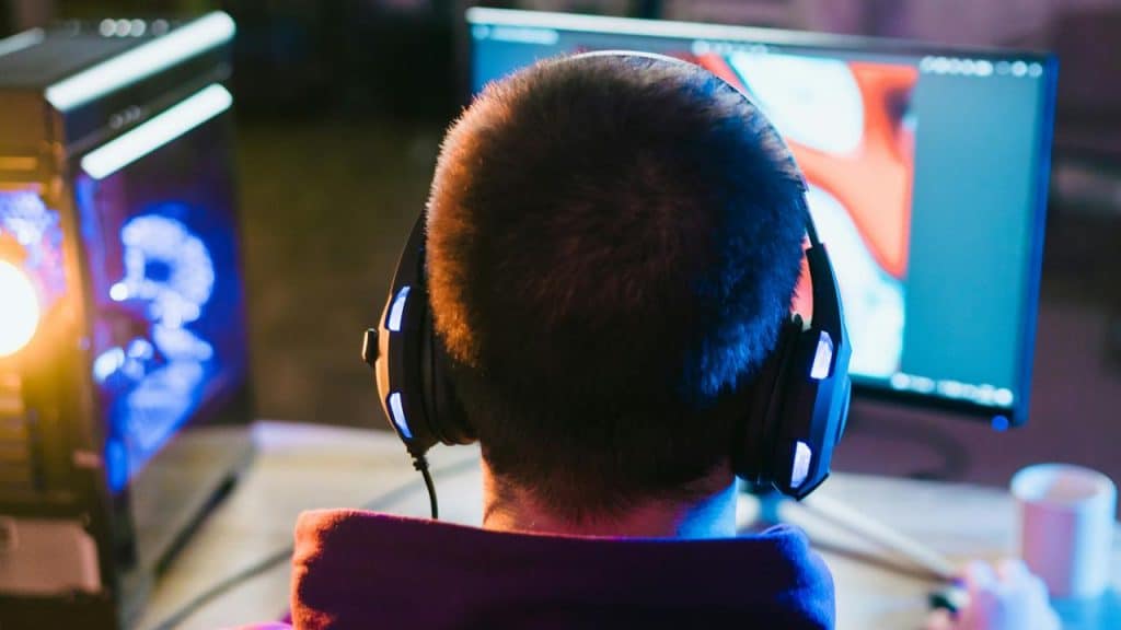 A person wearing headphones while working at a computer with glowing screens.