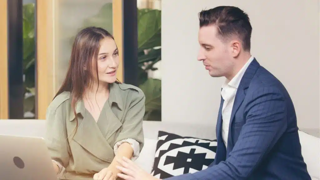 A woman in a green jacket and a man in a blue suit sit talking.