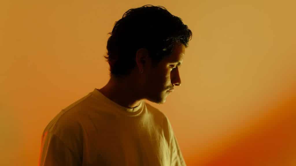 A man in a white t-shirt is shown in silhouette against a warm orange background.