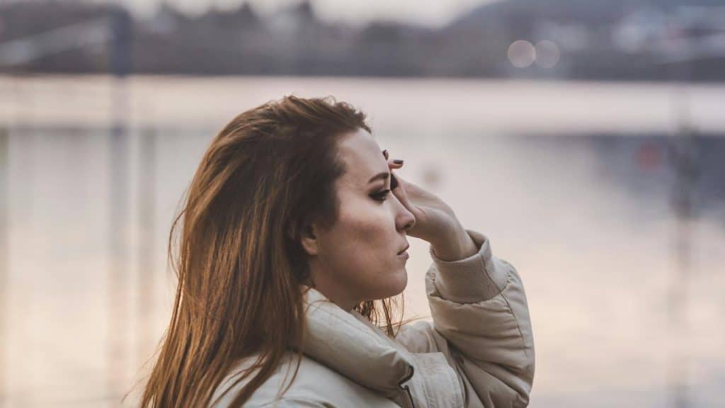 A person in a jacket gazing thoughtfully across a calm body of water.