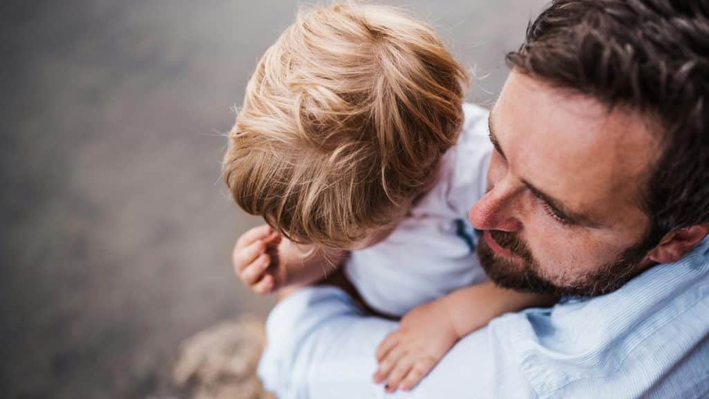 A father cradling a young child by the water.