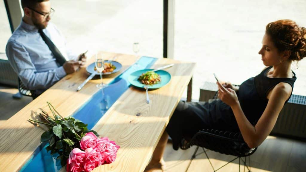 A couple sitting at a restaurant table, both looking at their phones.
