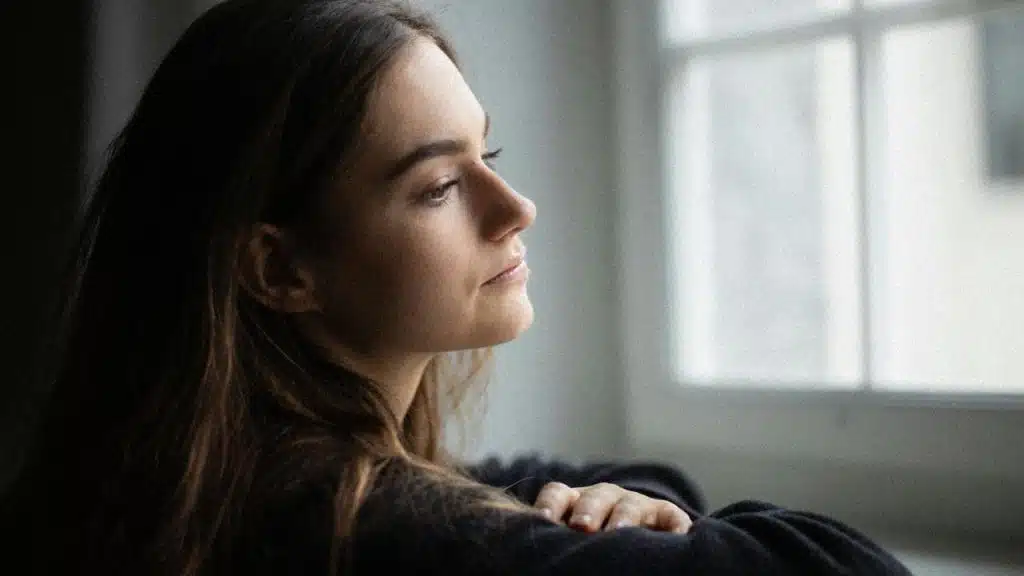 A person leaning by a window and gazing outside in quiet reflection.