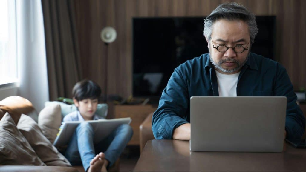 A man using a laptop while his son doing his homework