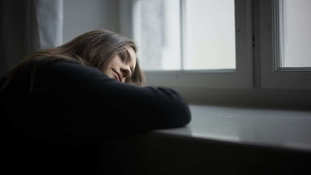 A woman leans her head on her arms while looking out of a window.