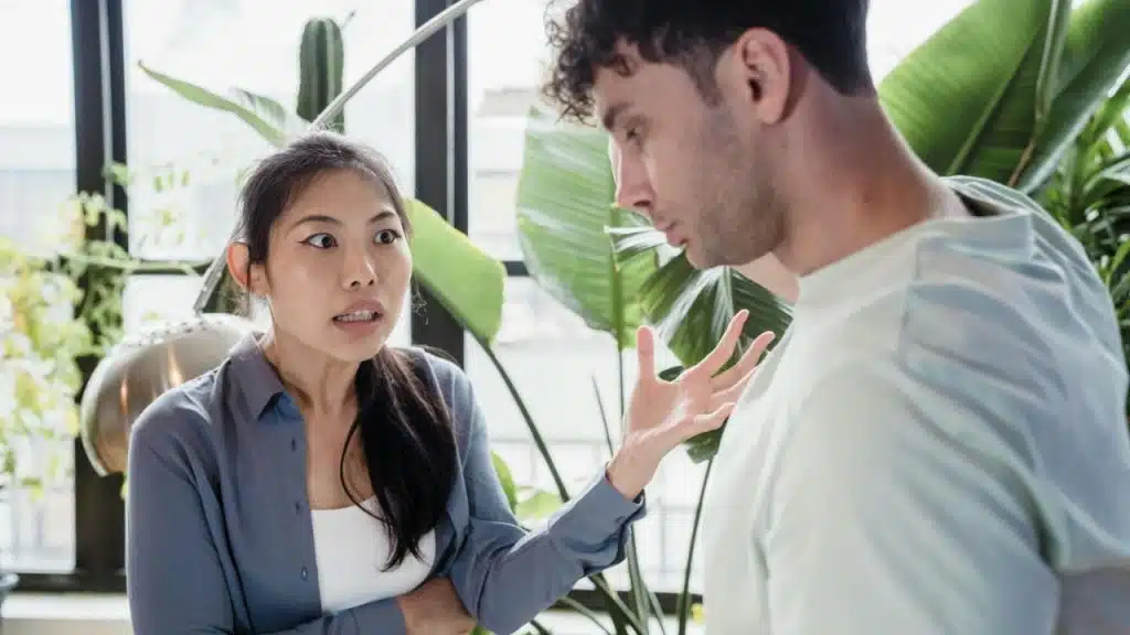 A woman with an intense expression gestures toward a man standing in front of her.