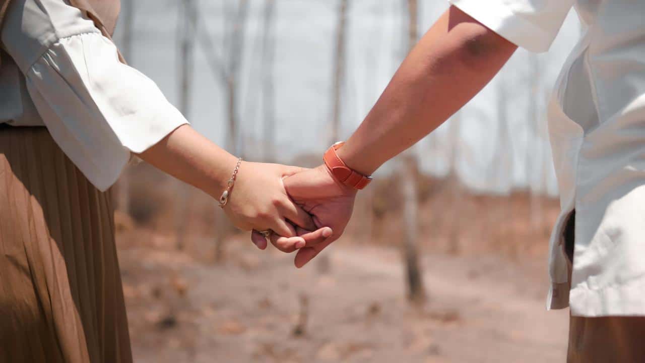 A close-up of a couple holding hands while standing in a dry, outdoor setting.