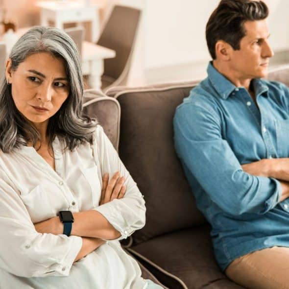 A man and woman sit on a couch with arms crossed, looking away from each other.