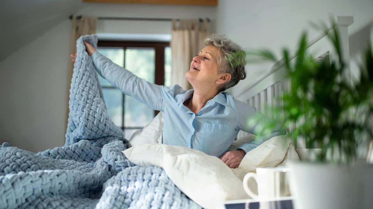 An older woman stretching in bed in the morning.