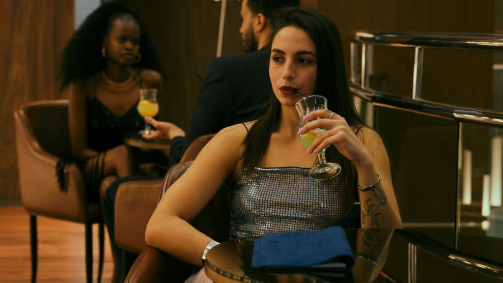 A woman in a sparkly top sips a drink through a straw while sitting at a table.