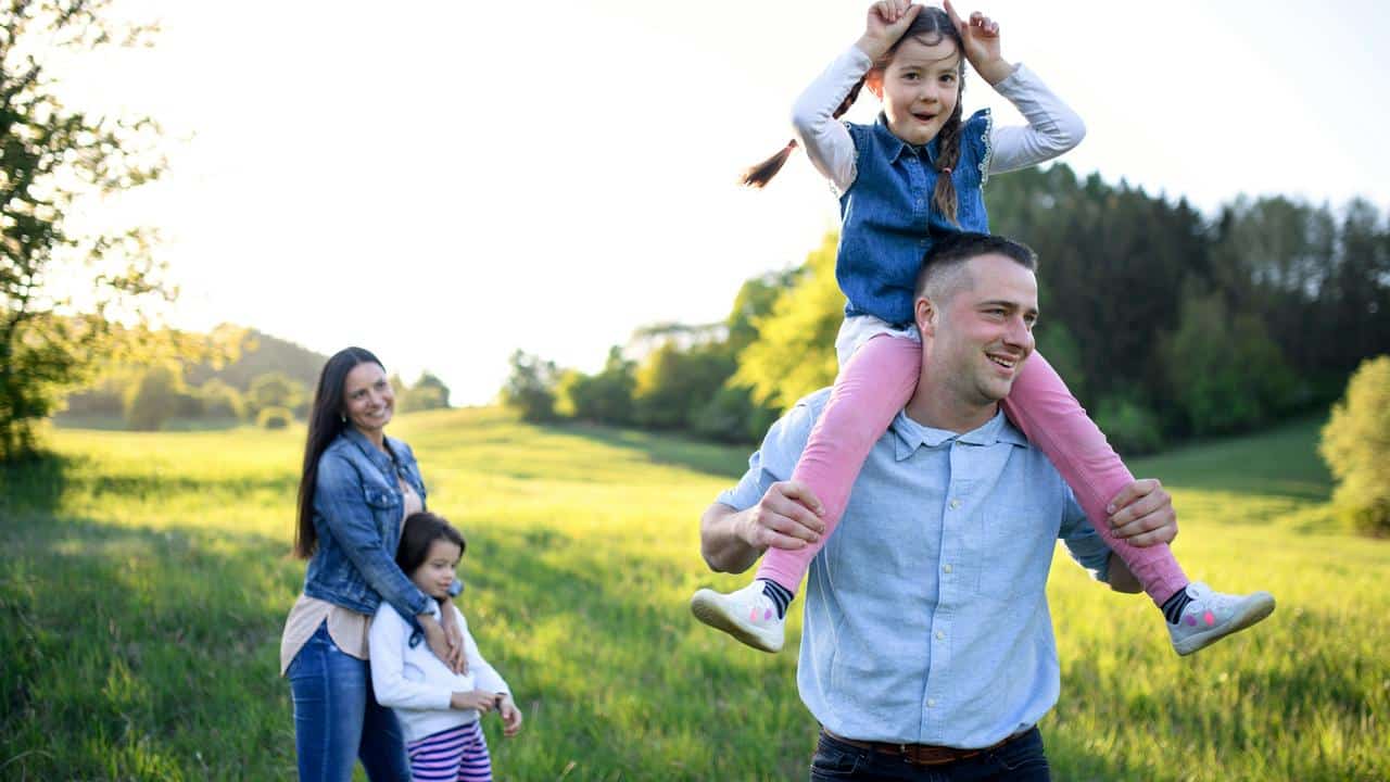 A father carrying a daughter on his shoulders while the mother and younger daughter stand behind.