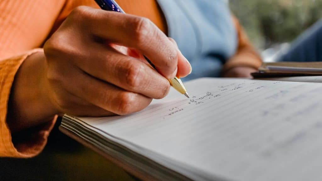 A hand writing notes in a lined notebook.